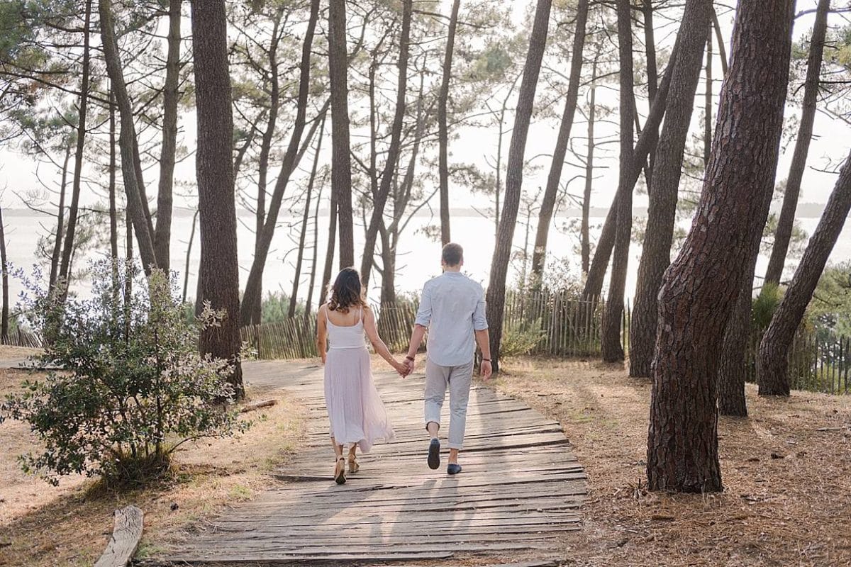 seance couple ou les futurs mariés marchent de dos avec une vue sur le bassin d'arcachon en pleine foret