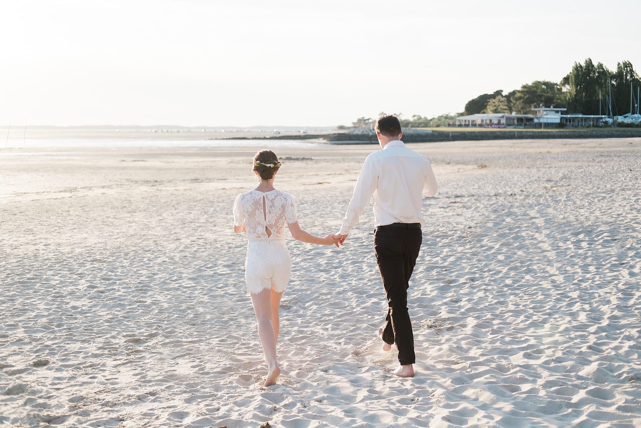 seance couple ou les futurs mariés sont en train de courir sur la plage de dos au bord du bassin d'arcachon avec un photographe de mariage