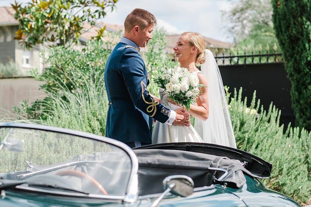 Les mariés se regardent avec le sourire aux lèvres devant une belle voiture