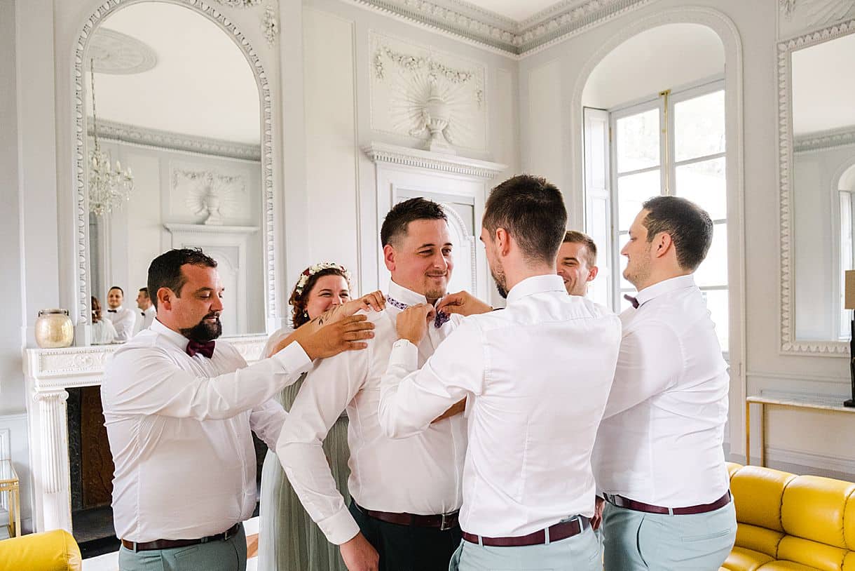 mise en place du noeud papillon sur le marié avec l'ensemble des témoins autour de lui au chateau de l'hospital