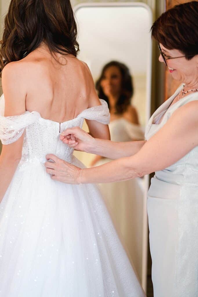 la maman de la mariée est en train de remonter le fermeture éclair de sa robe