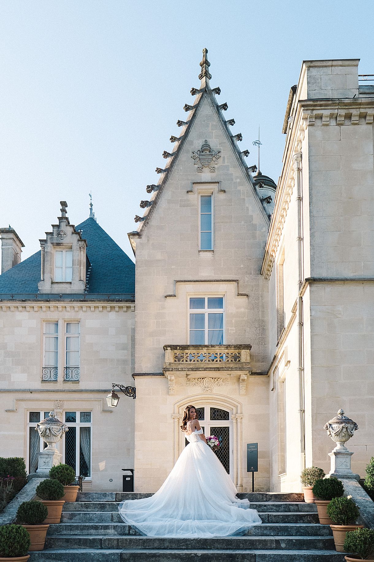 la mariée est de dos en train de regarder le photographe sur les escaliers du château pape clément