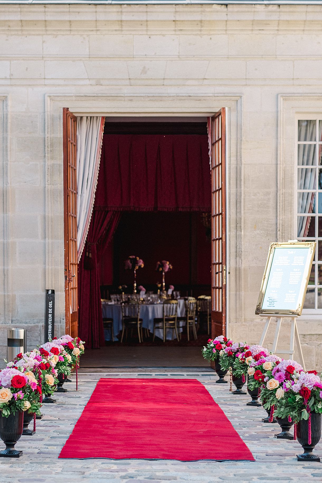 vue d'ensemble sur l'entrée de la réception avec un tapis rouge et des bouquets de fleurs sur chaque côté au château pape clément