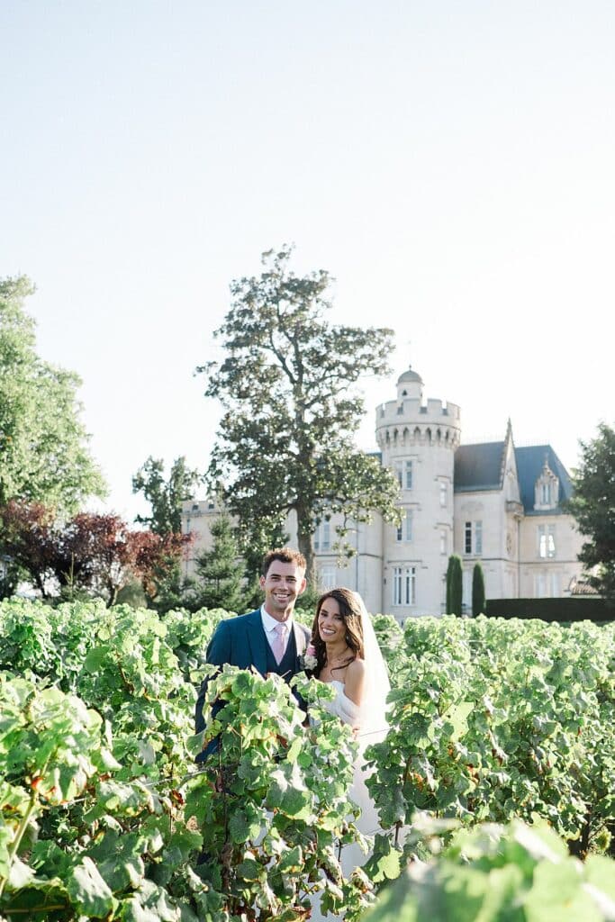 le couple de mariés sont enlacés en regardant le photographe avec un grand sourire et le château pape clément en arrière plan