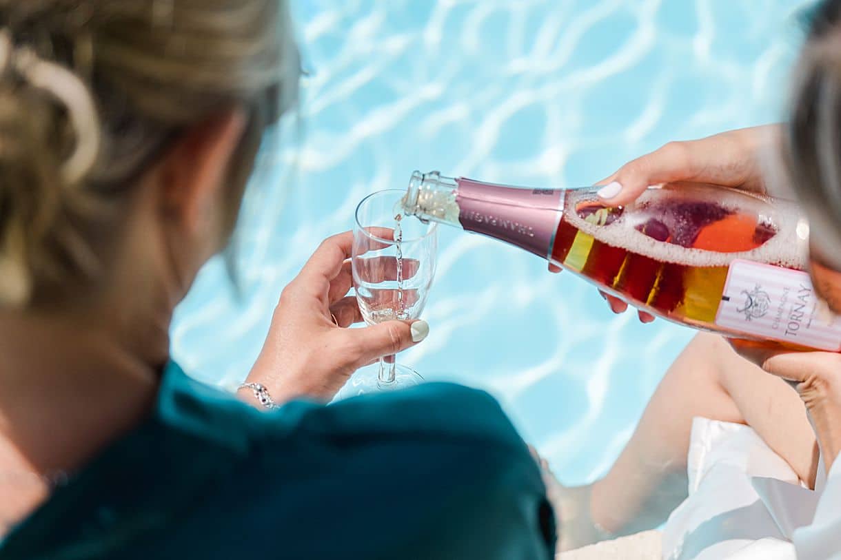 la témoin sert la mariée une coupe de champagne lors de ses préparatifs au bord de la piscine