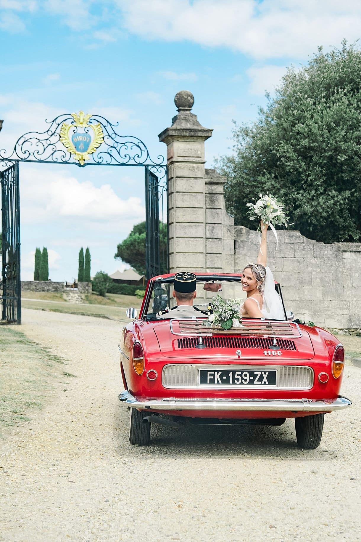 la mariée s'est retourné dans sa voiture en train de regarder le photographe pixaile photography et lève son bouquet de fleurs au portail du chateau de birot à beguey