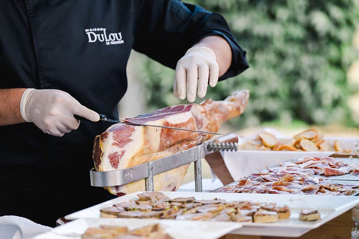 le traiteur dulou découpe le jambon pendant le mariage de marine et louis au chateau de birot pendant le cockail