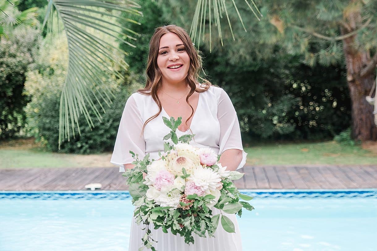 portrait de la mariée souriante avec son bouqet de fleurs autour de la piscine