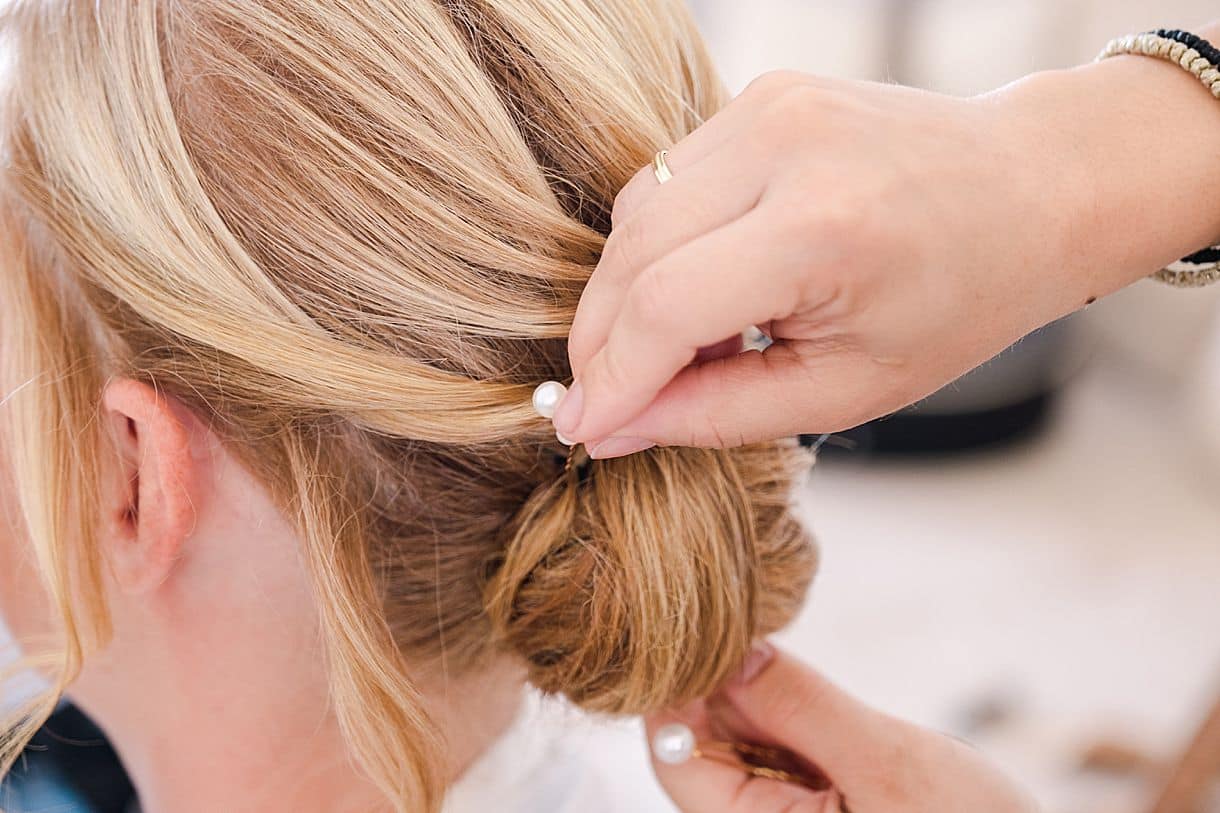 la coiffeuse termine de mettre les bijoux dans les cheveux de la mariée pour son mariage en crête