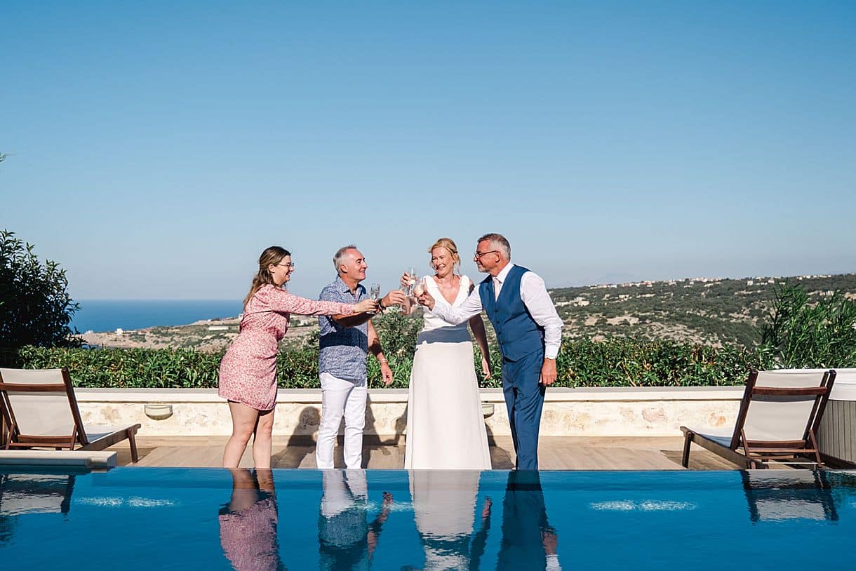 les mariés sont en train de trinquer une coupe de champagne dans une villa de luxe avec les témoins devant leur piscine avec une vue imprenable sur la crete