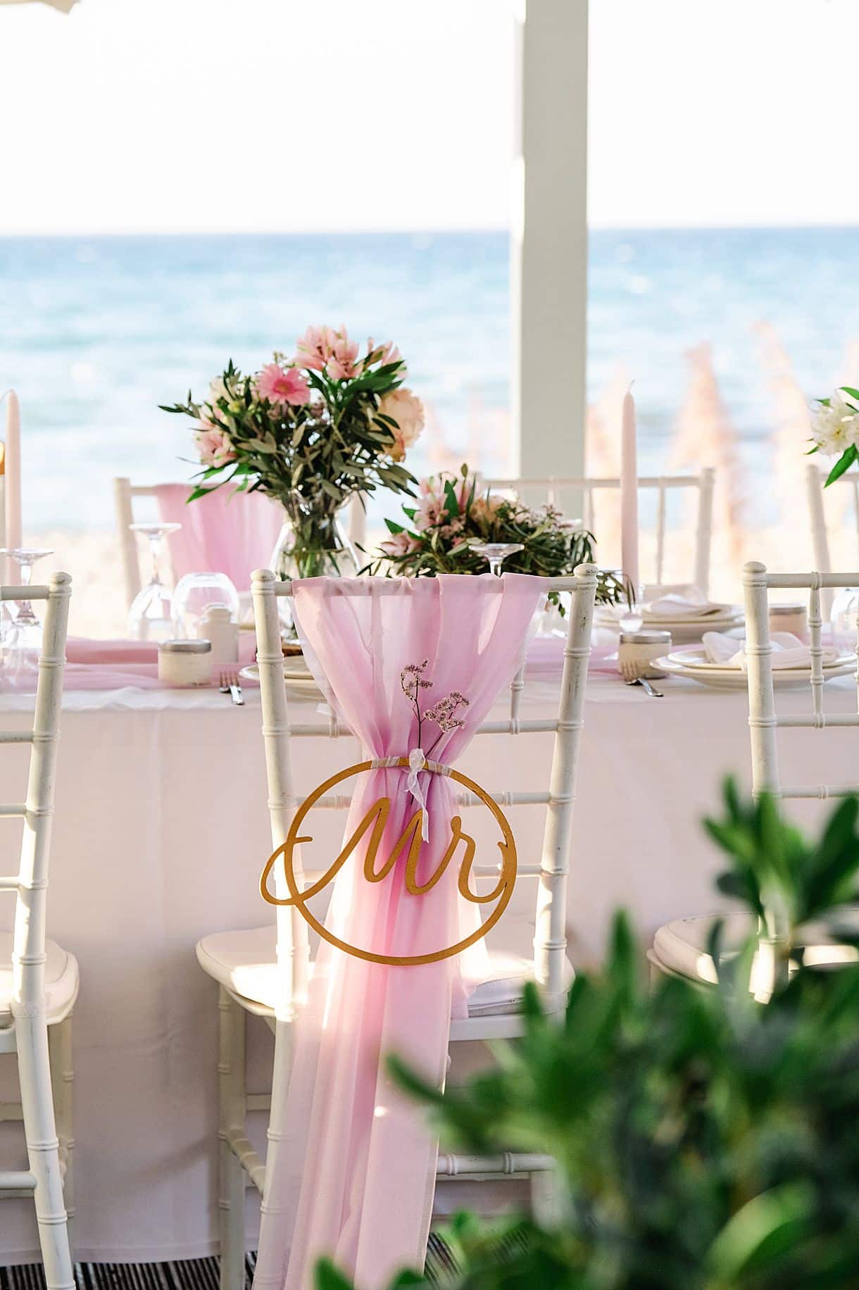 détail de la chaise du marié à la table de réception entouré d'un voile rose et écrit MR dessus. photos vue sur la plage en crête