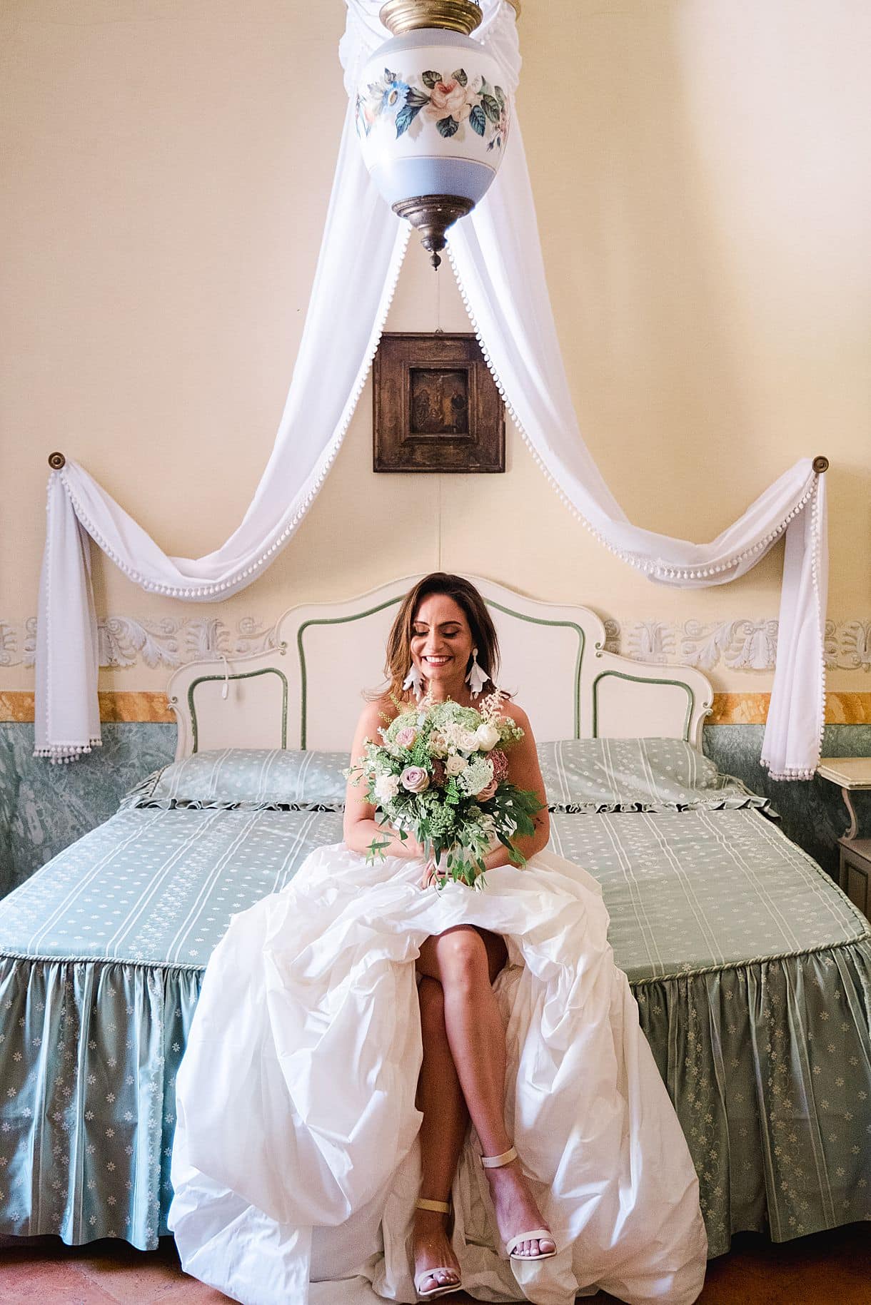 photo de la mariée sur le bord du lit avec son bouquet de fleurs